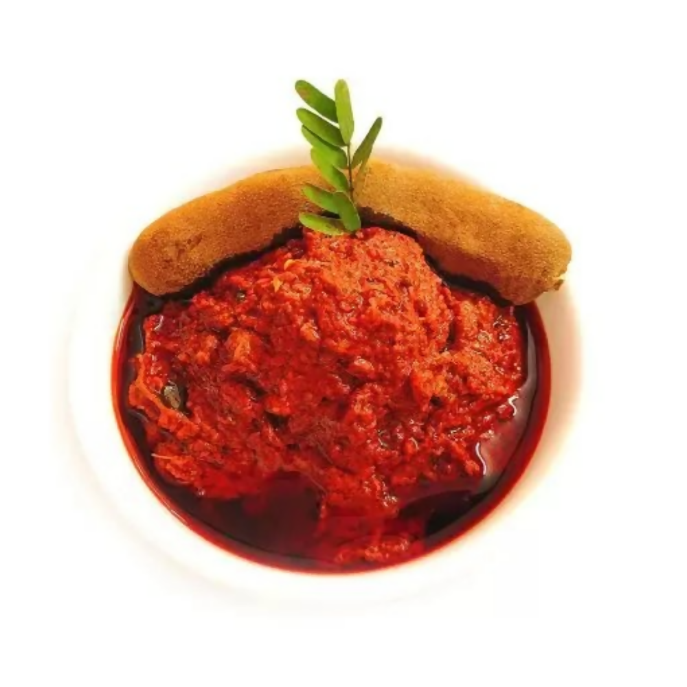 Red dip in a bowl with a bread roll on a white background