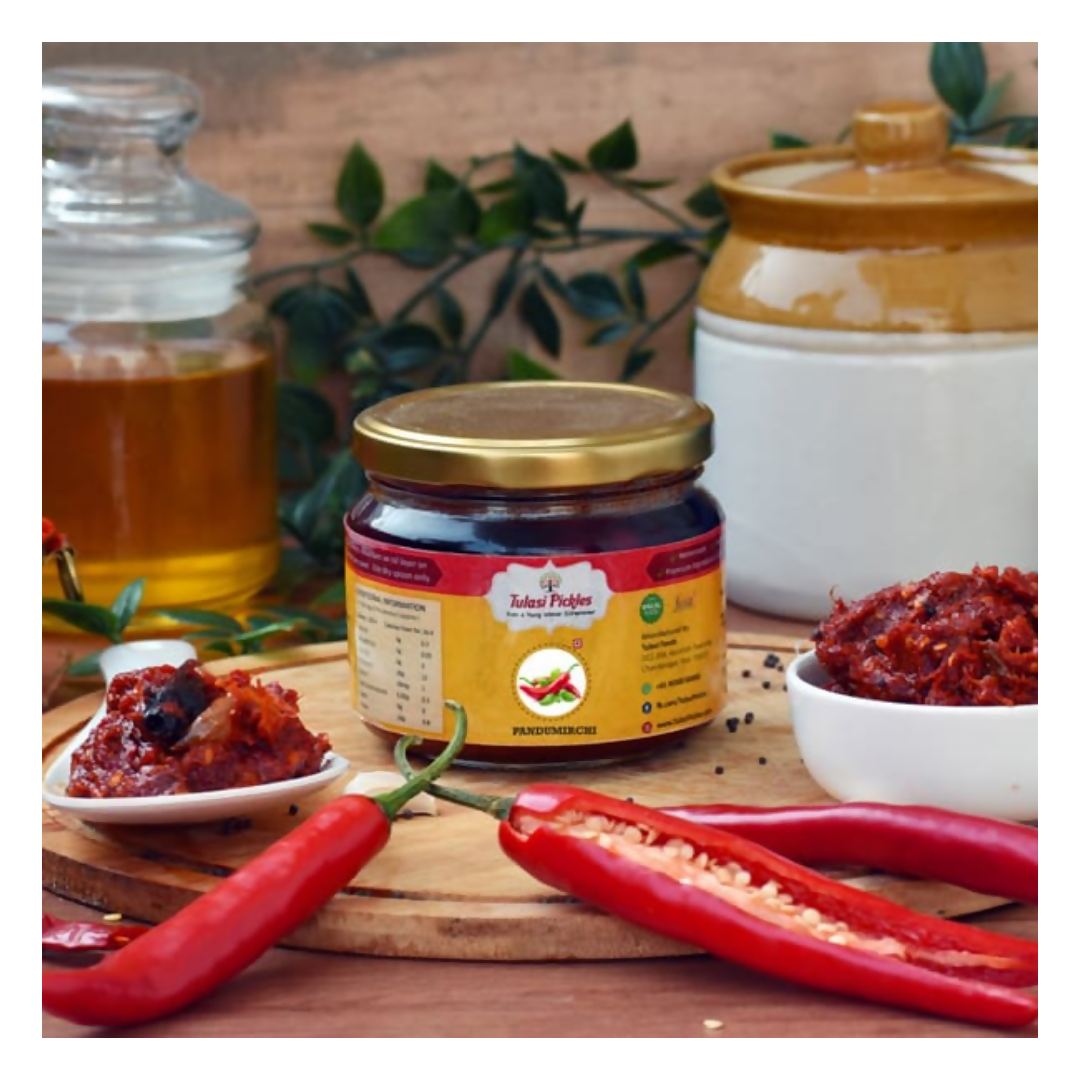 Jar of Tadka Prikhan with red chilies and a bowl of chutney on a wooden surface.