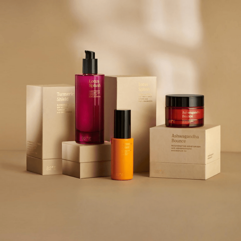 A collection of skincare products from 82°E by Deepika Padukone, including a cleanser, moisturizer, and sunscreen serum, displayed against a neutral background with Propylene glycol in a bottle.
