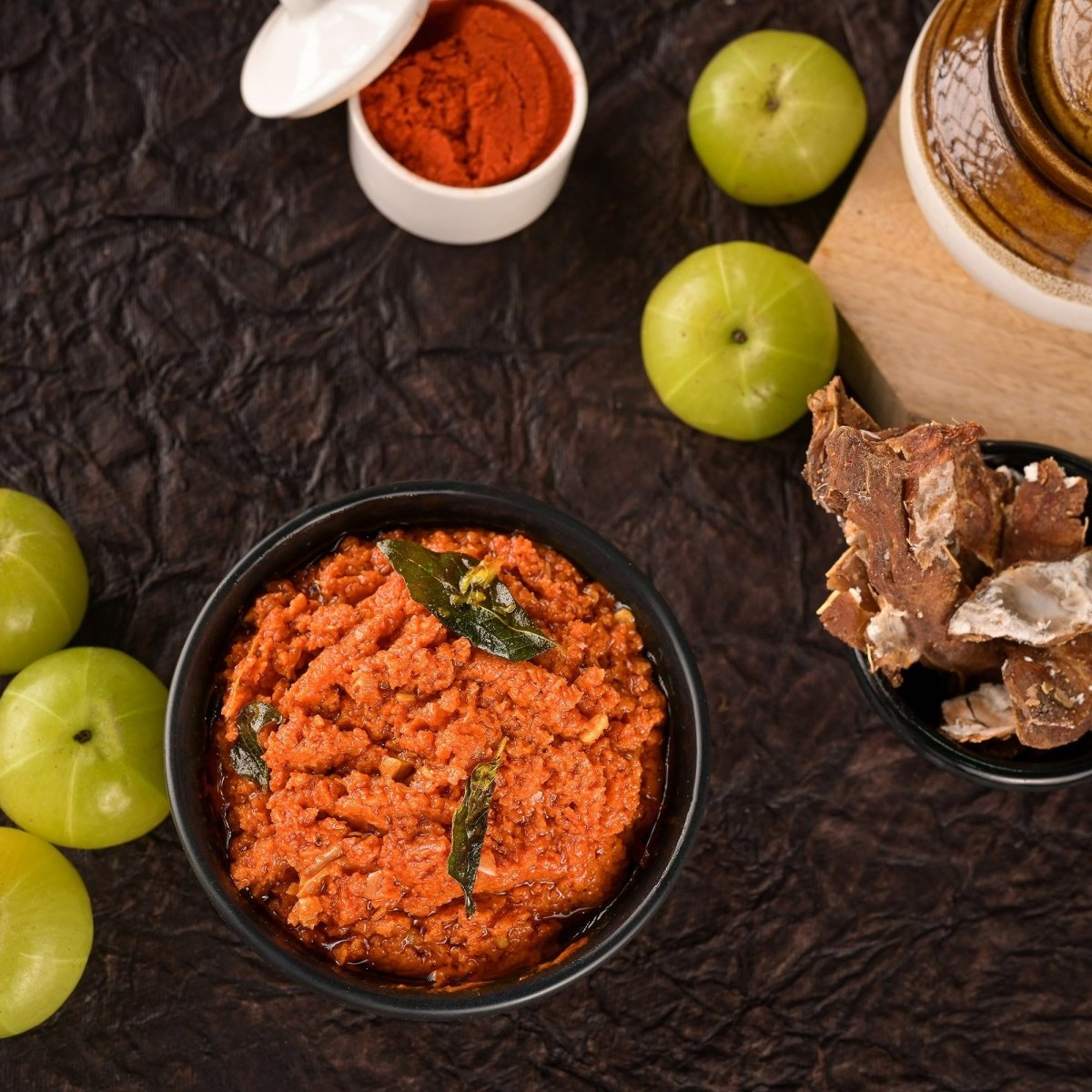 Bowl of red curry with green apples and a wooden container on a dark surface