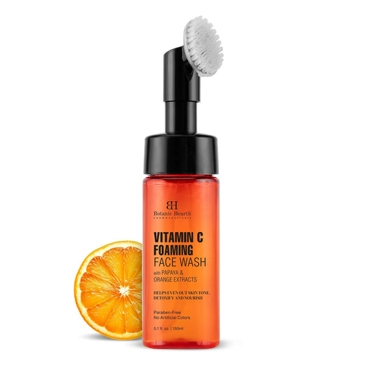 A bottle of Botanic Hearth Vitamin C Foaming Face Wash with Papaya & Orange Extracts, featuring a built-in brush and a slice of orange in the background.