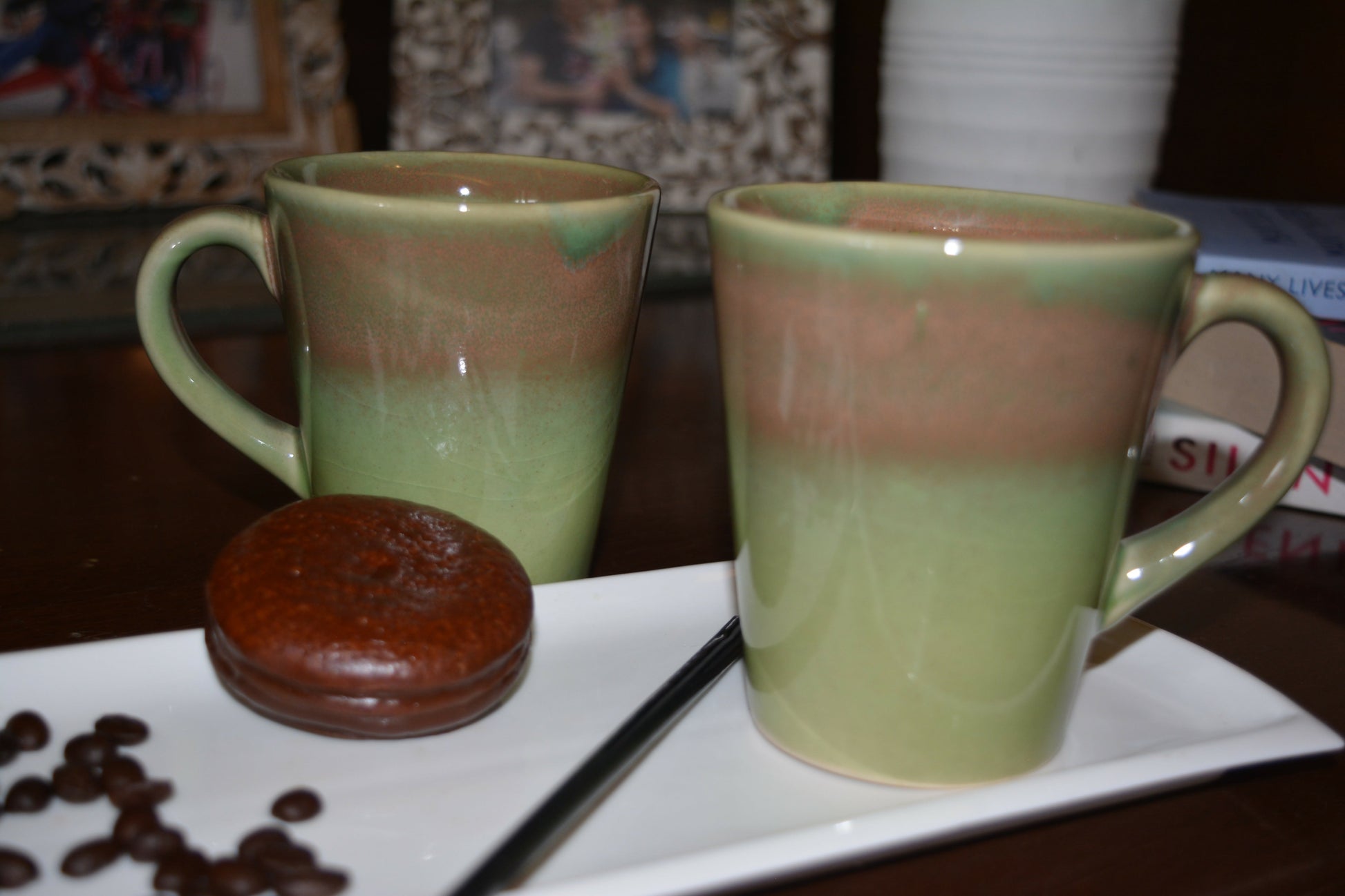 Two ceramic mugs with a gradient design on a white plate with coffee beans and a cookie.