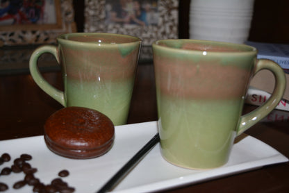 Two ceramic mugs with a gradient design on a white plate with coffee beans and a cookie.