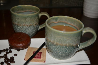 Two ceramic mugs with a beverage, a chocolate dessert, and coffee beans on a white plate.