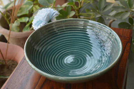 Green ceramic bowl on a wooden surface with plants in the background