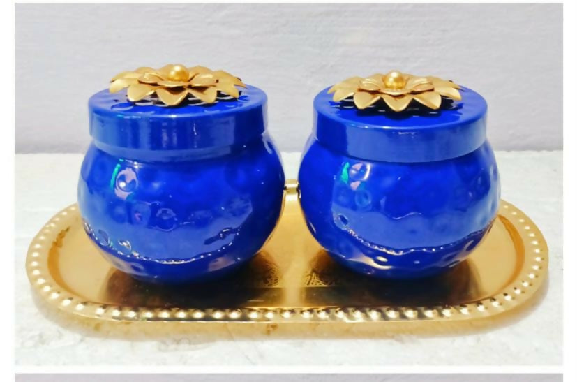 Two blue ceramic pots with gold lids on a gold tray against a light gray background