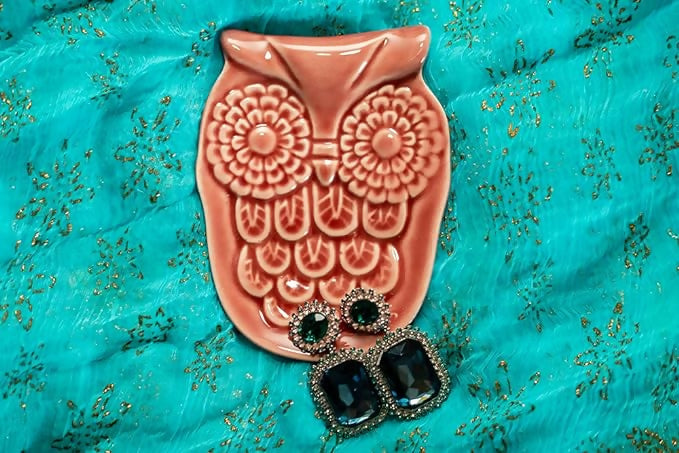 Decorative owl-shaped object with black gemstones on a turquoise fabric background