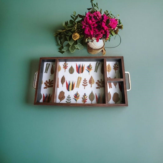 Wooden tray with floral patterns on a teal wall with a vase of flowers.