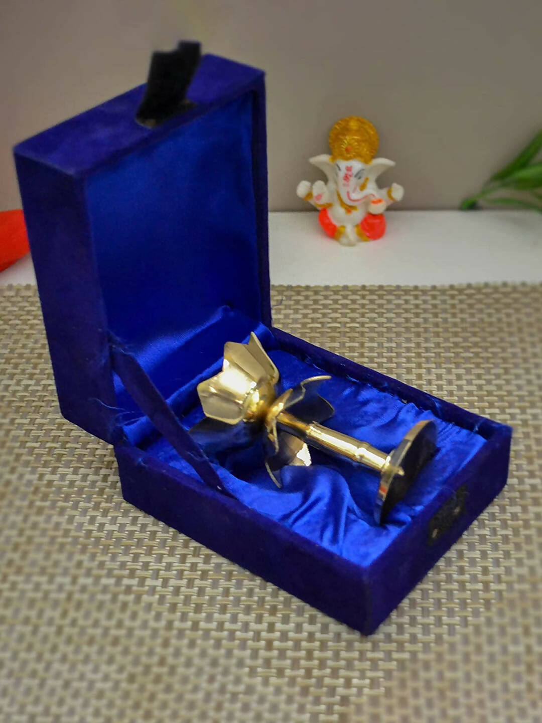 Gold-colored object in a blue velvet box on a textured surface with a small figurine in the background.