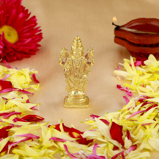 Gold-colored deity statue on a bed of flowers with a lit candle in the background