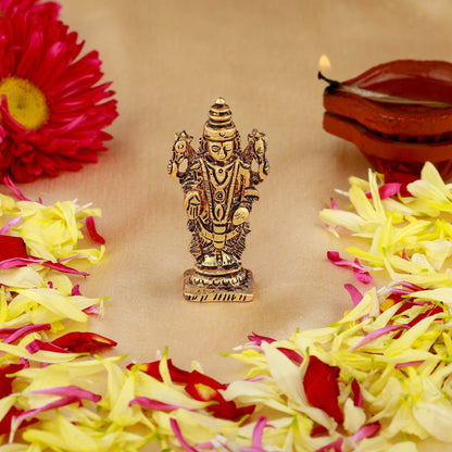 Decorative statue of a deity surrounded by flowers and a lit lamp on a beige background