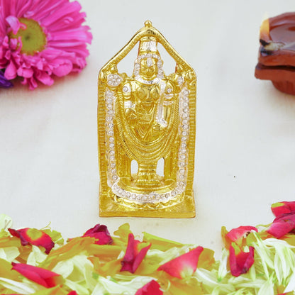 Gold-colored deity statue on a white surface with flowers and petals.