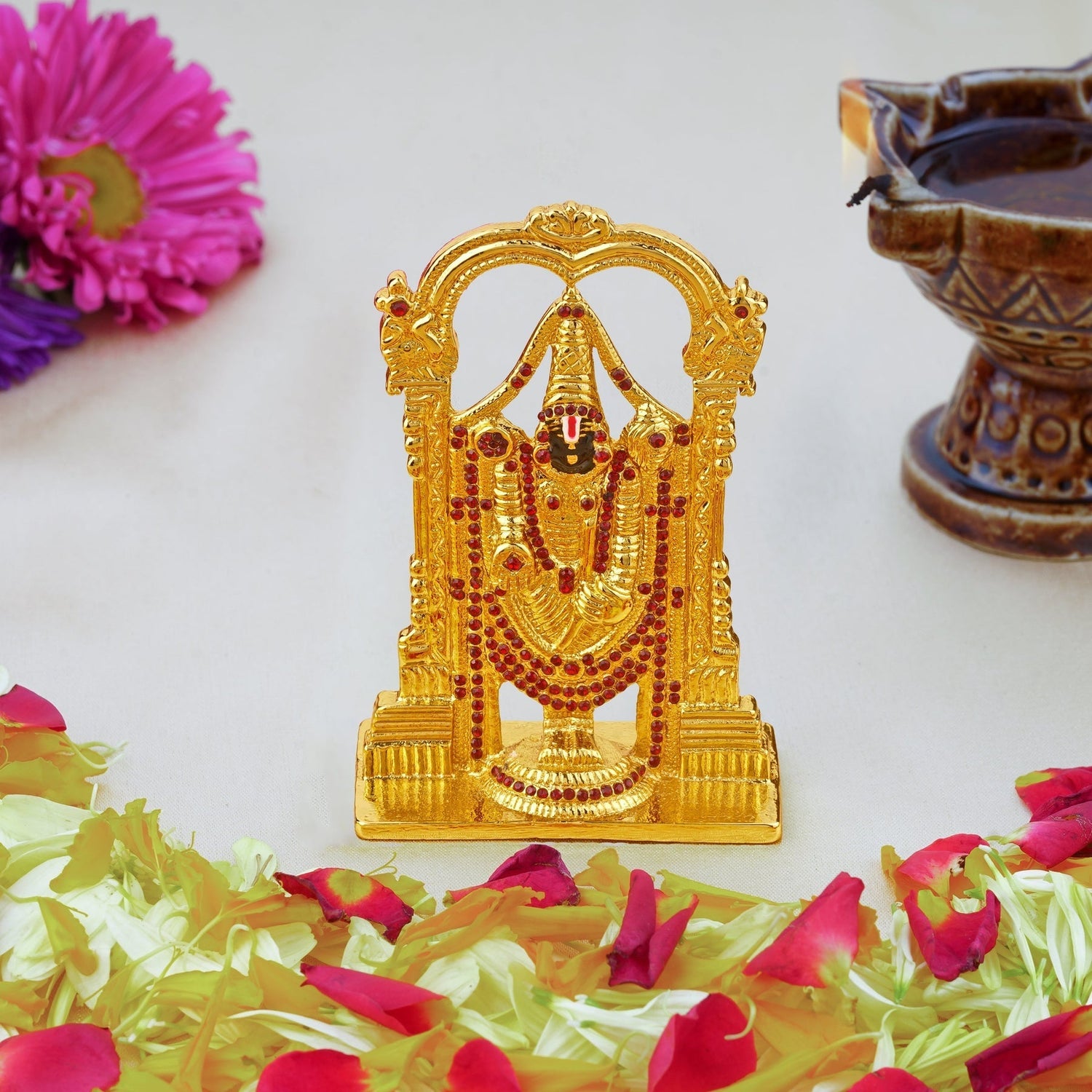 Gold-colored deity statue with flowers and a lamp on a white background