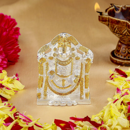Decorative metal idol with gold accents on a table with flowers and a lit lamp.