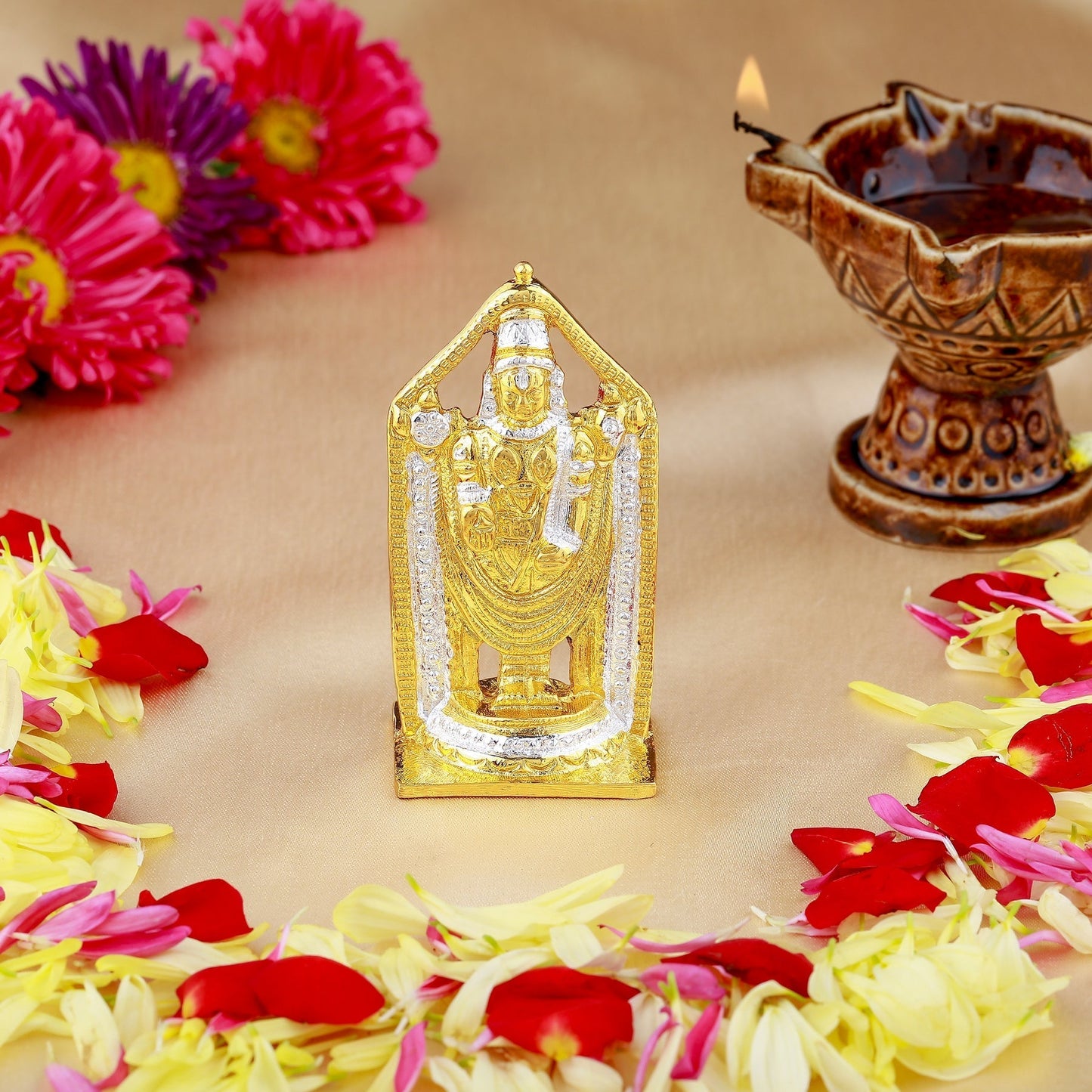 Decorative statue with flowers and a lit oil lamp on a beige surface