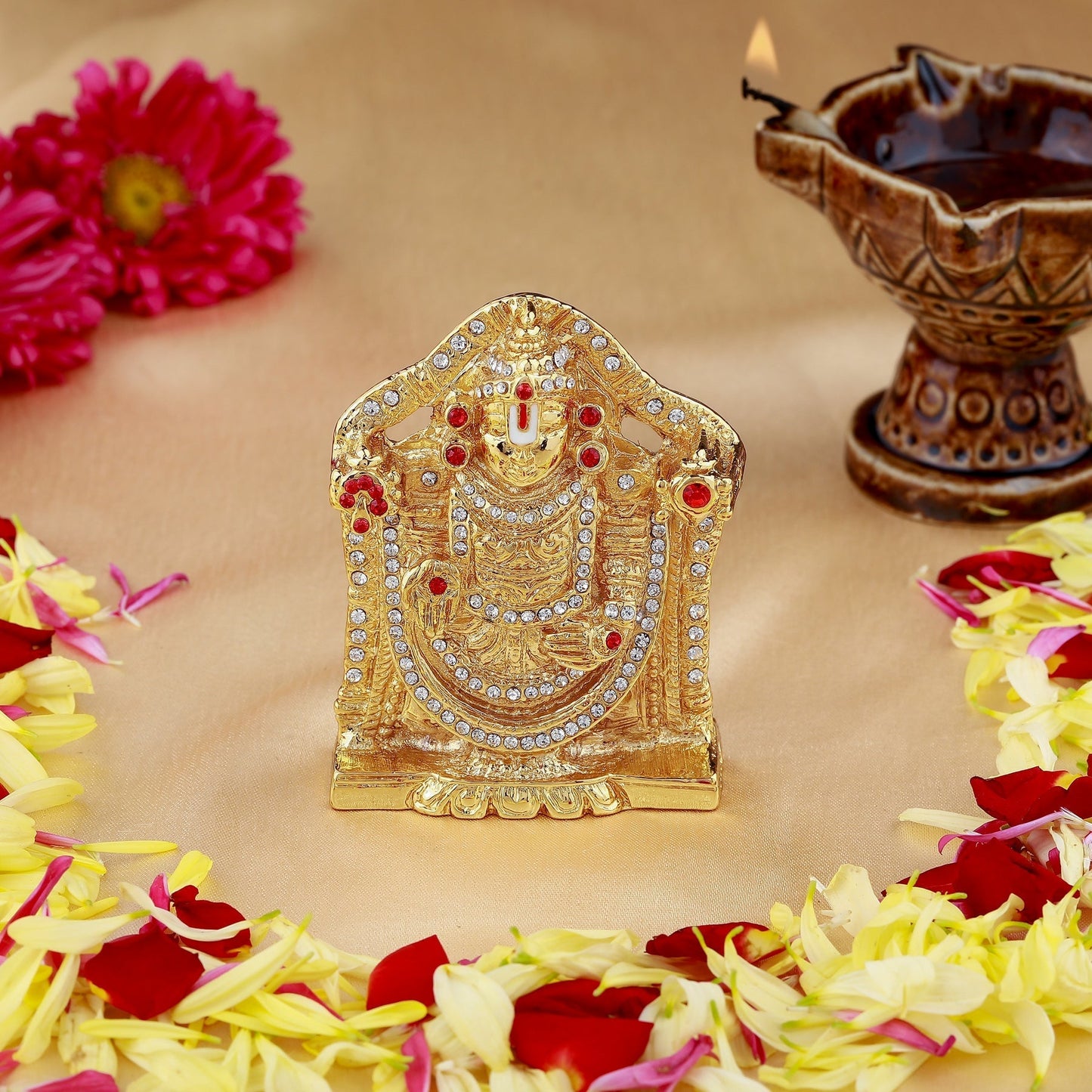 Decorative gold idol with flowers and a lamp on a beige background