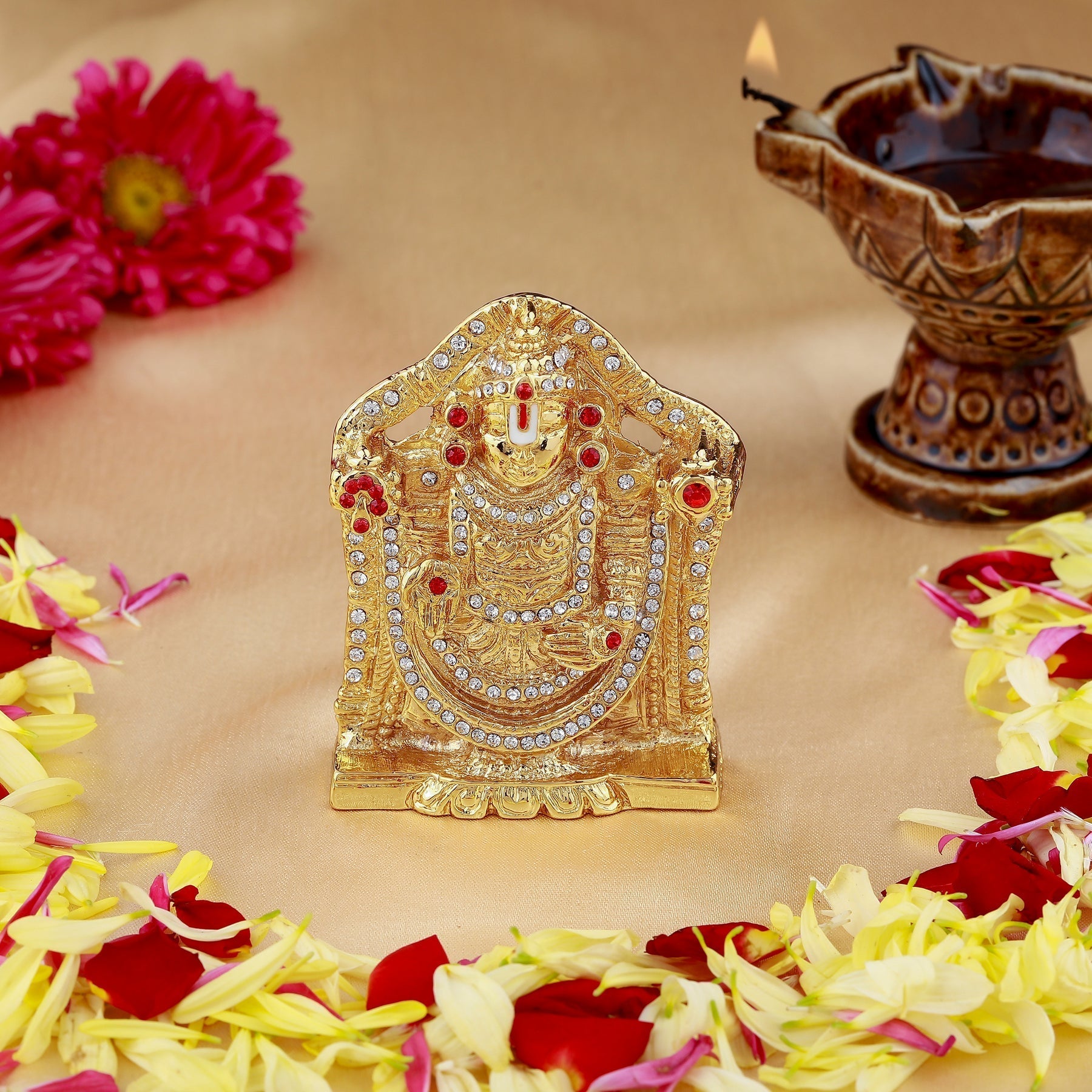 Decorative gold idol with flowers and a lamp on a beige background