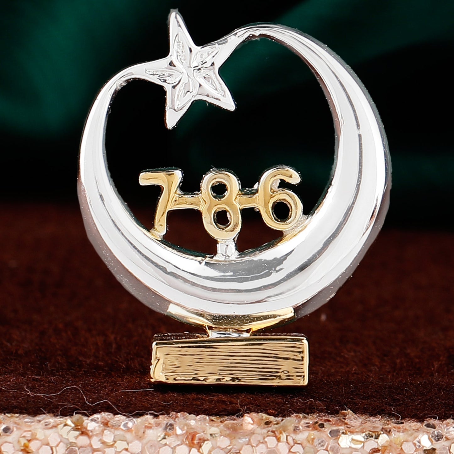 Decorative item with a silver crescent moon and star, gold number '786', and textured base on a dark background.