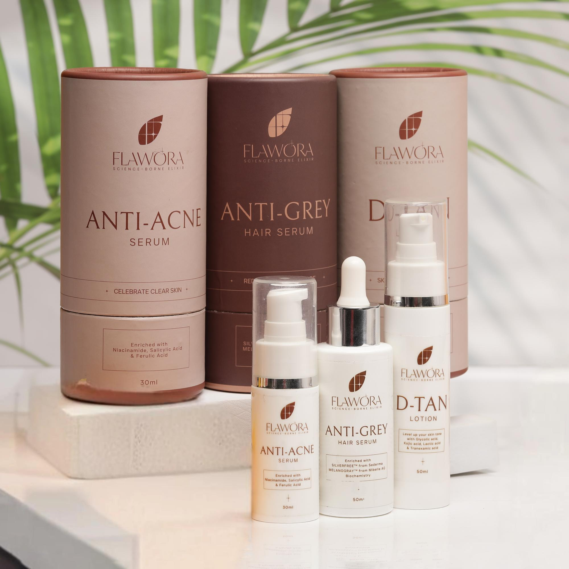 Flawora skincare products including serum, hair serum, lotion, and dropper on a white surface with green leaves in the background.