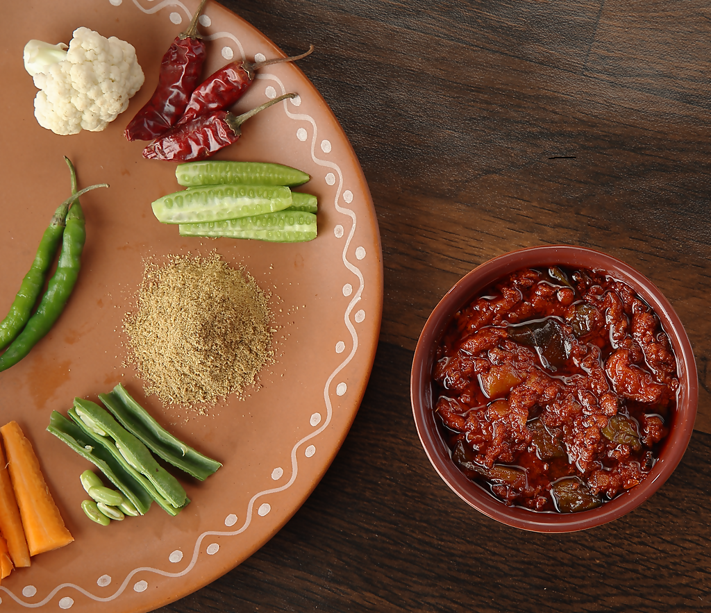 Dish with ingredients and a bowl of red curry on a wooden surface