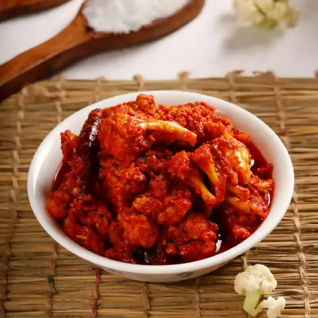 Bowl of spicy food on a woven mat with a wooden spoon and salt in the background.