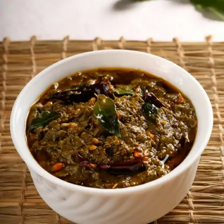 White bowl of green curry with herbs on a woven mat