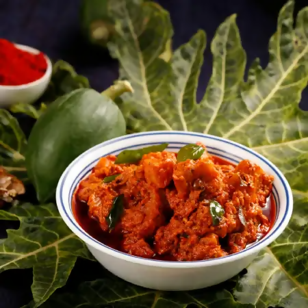 Bowl of red curry with green leaves on a dark background