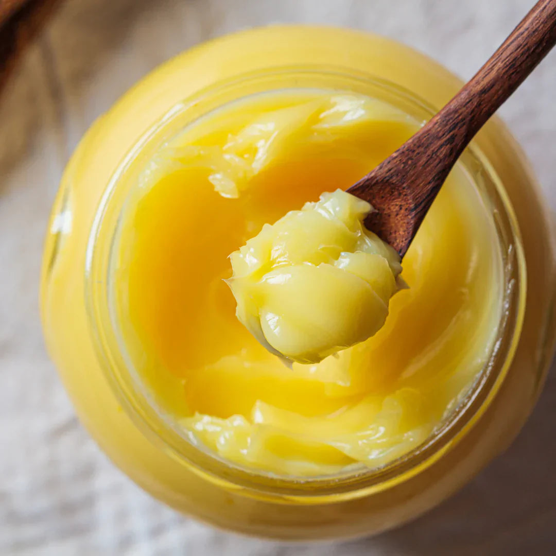 Jar of yellow butter with a wooden spoon lifting some out, on a light background