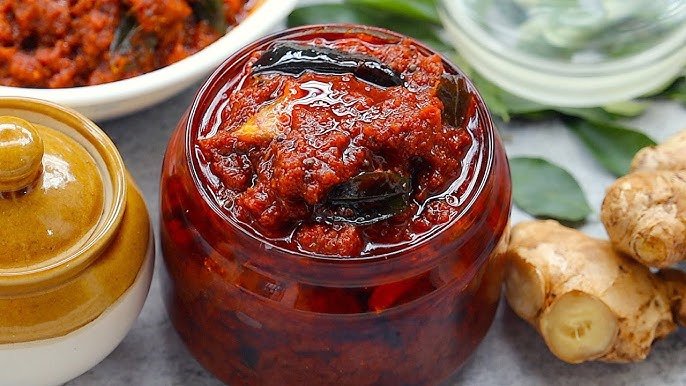Jar of red chutney with a lid on a table with ingredients