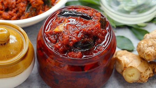 Jar of red chutney with a lid on a table with ingredients