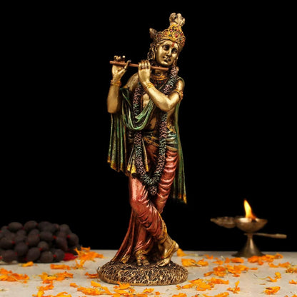 Statue of a deity holding a flute with flowers and a lamp in the background
