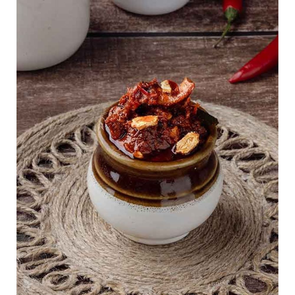 Small ceramic jar with a lid filled with a spicy-looking dish on a textured surface.
