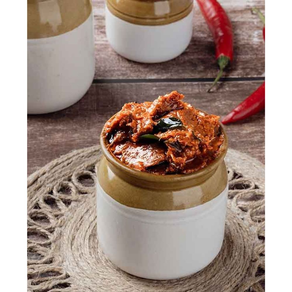Jar of red curry paste on a wooden surface with red peppers.