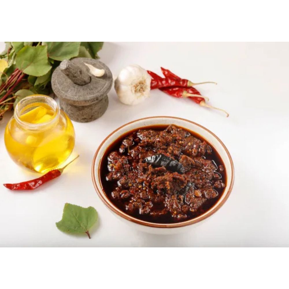 Bowl of dark sauce with oil, garlic, and red peppers on a white background
