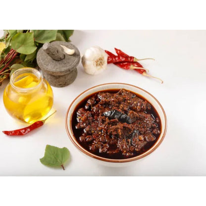 Bowl of dark sauce with oil, garlic, and red peppers on a white background