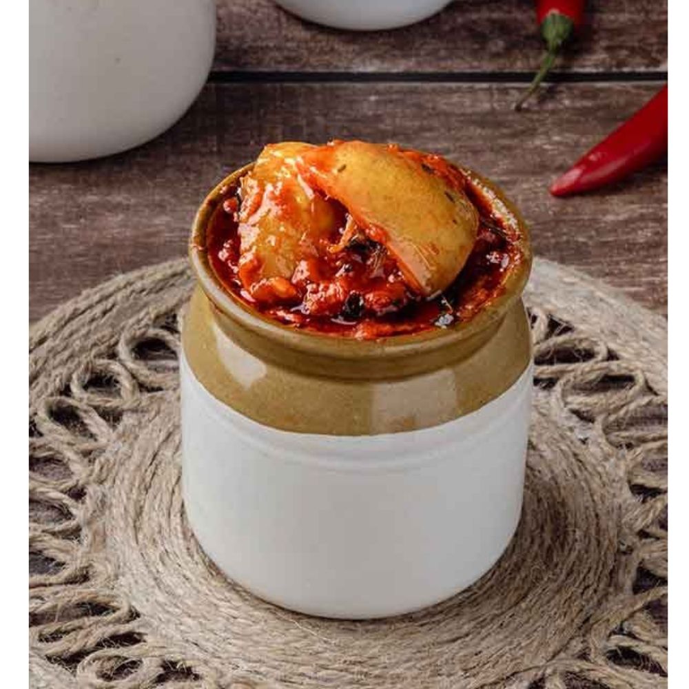 Ceramic jar with a lid containing a red substance on a woven mat.