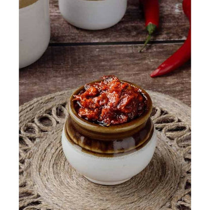 Small ceramic jar with red chili paste on a woven mat with red chilies in the background