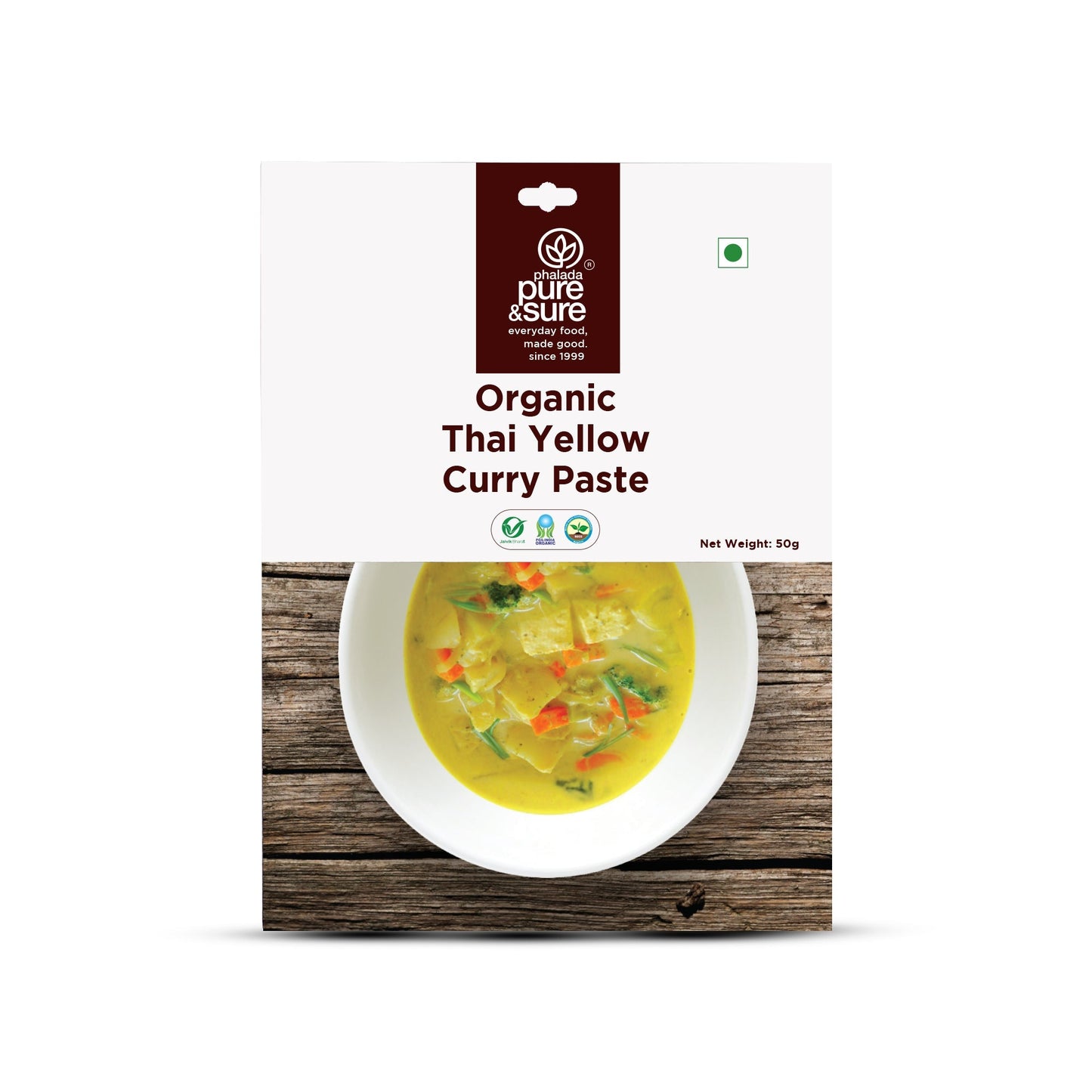 Package of pure & sure Organic Thai Yellow Curry Paste with a bowl of curry on a wooden background