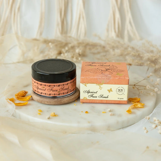 Jar of apricot face scrub with packaging on a marble surface with dried apricots and flowers.