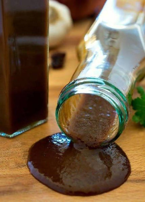 Glass bottle with a green cap spilling dark liquid onto a wooden surface