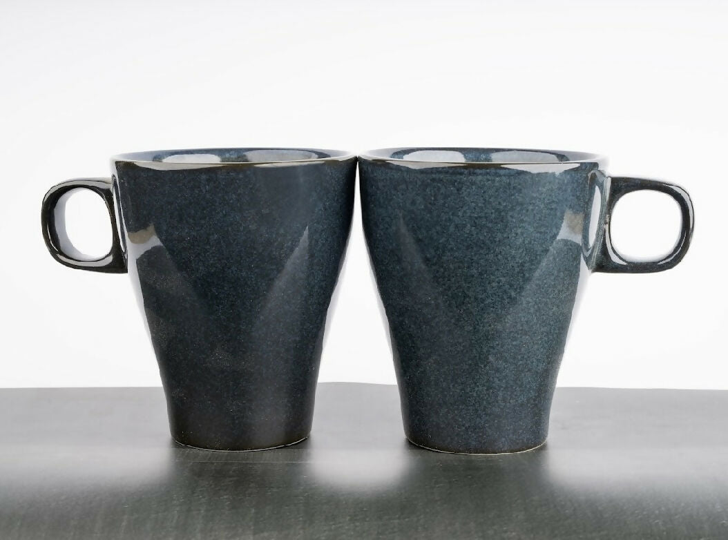 Two blue ceramic mugs on a reflective surface with a white background