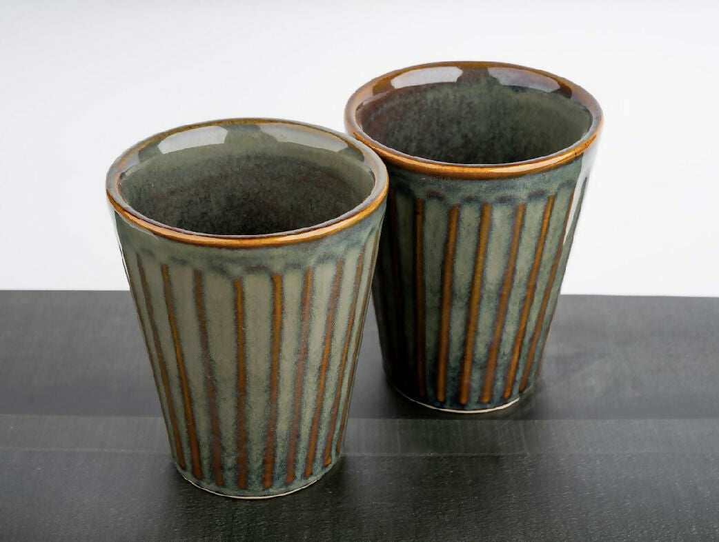 Two ceramic cups with striped design on a dark surface