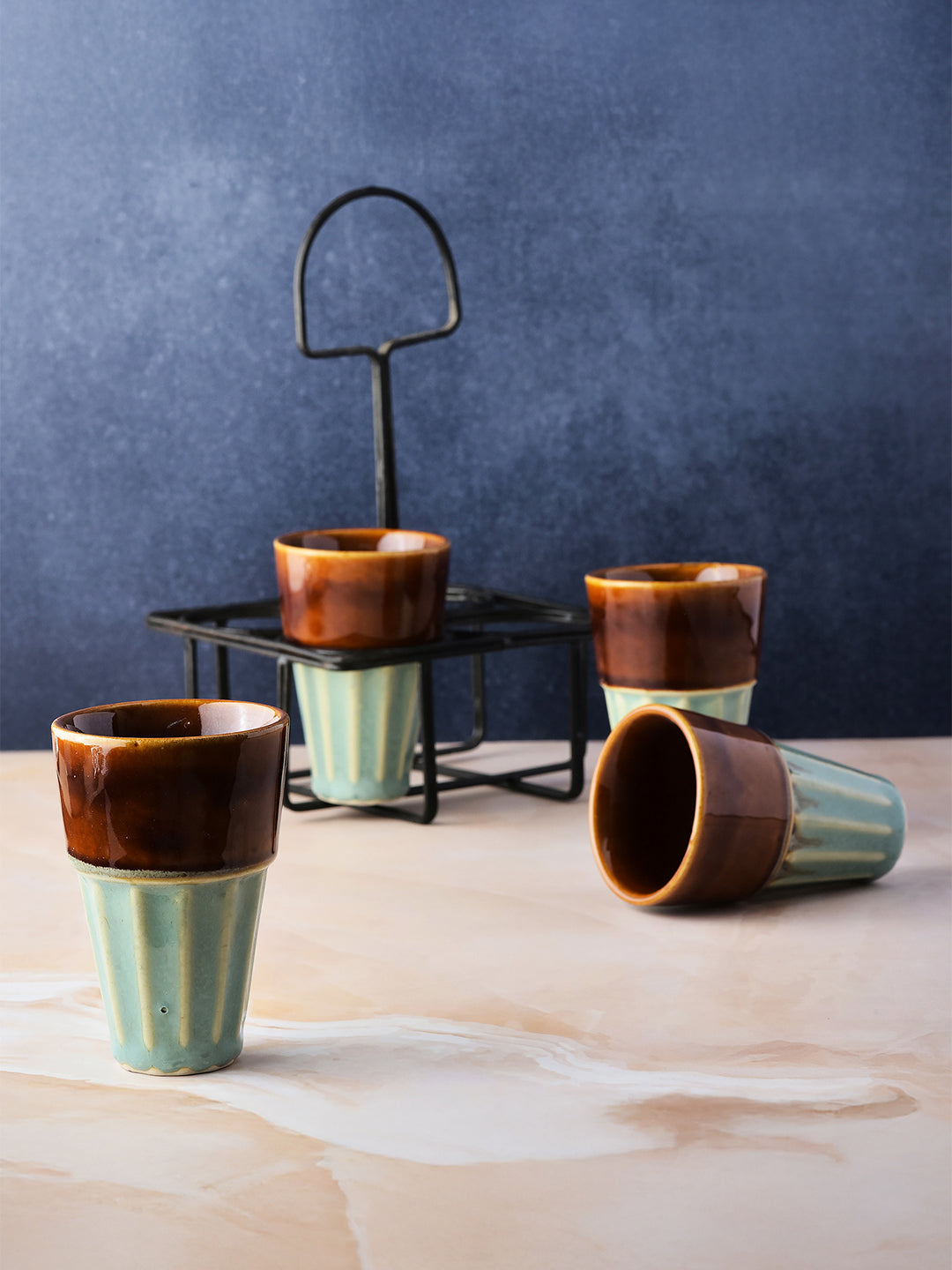 Set of ceramic cups with brown and green glaze on a wooden surface against a blue wall.