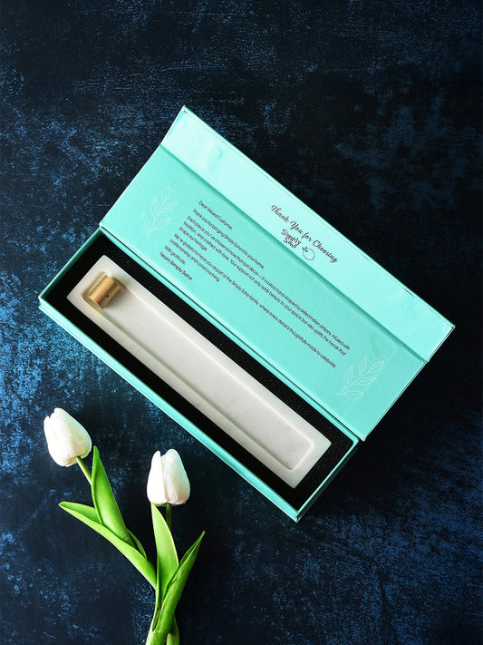 White ceramic object in a teal box on a dark textured surface with white tulips.