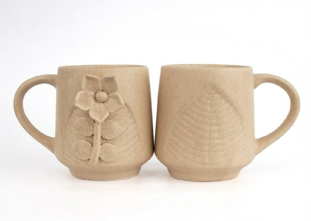 Two beige ceramic mugs with floral designs on a white background
