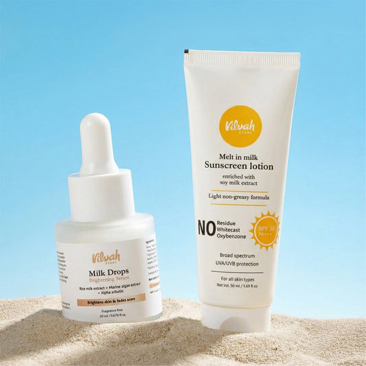 Two skincare products, a dropper bottle and a tube of sunscreen lotion, on a sandy surface with a clear blue sky.