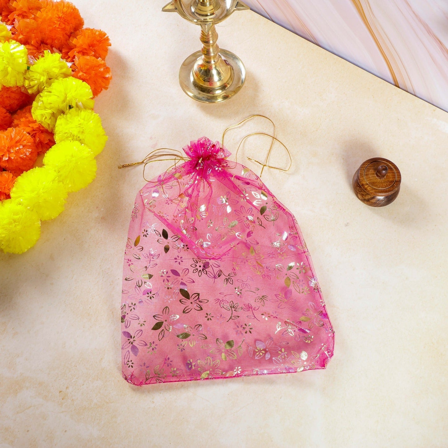 Pink floral-patterned organza bag on a marble surface with decorative items.