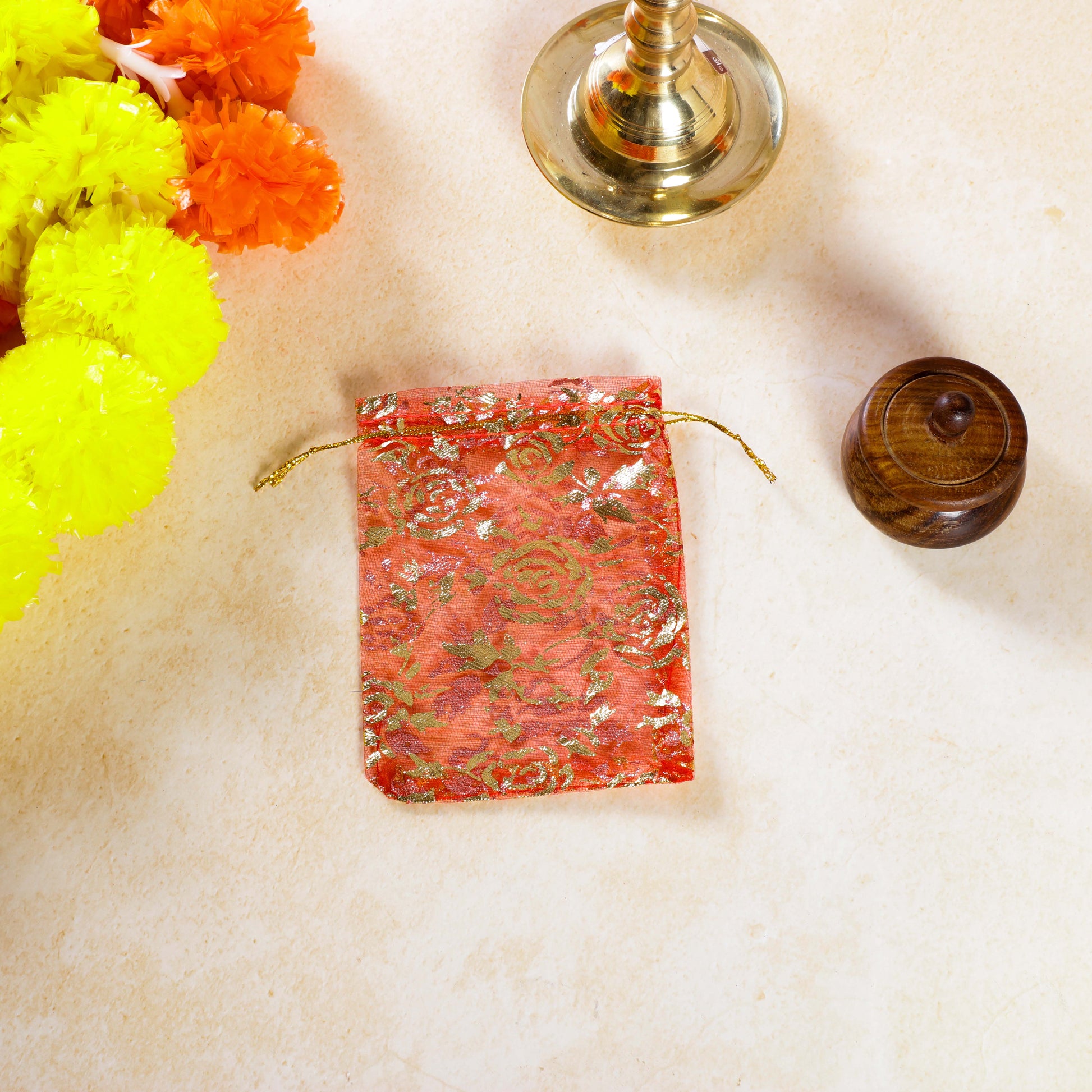 Decorative red pouch with gold patterns on a light beige surface with flowers and a small wooden object.