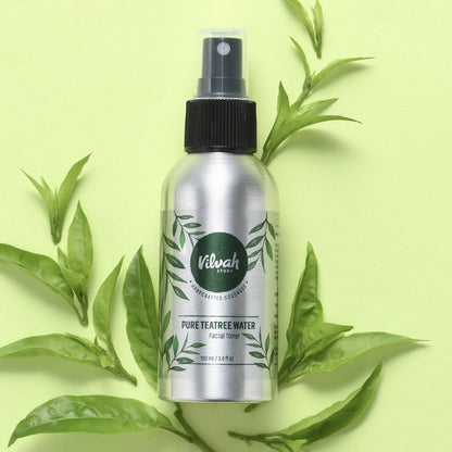 Silver bottle of Viluh Store Pure Teatree Water with black spray nozzle on a light green background with tea leaves.