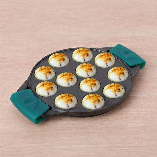 Small frying pan with green handles containing round fried items on a beige surface